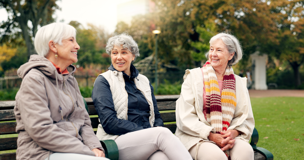 Group of three, female seniors sitting on bench, smiling.