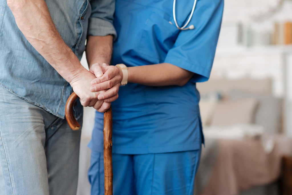 Close up shot of seniors hands on cane, caregivers hands on top of seniors, assisting walk.